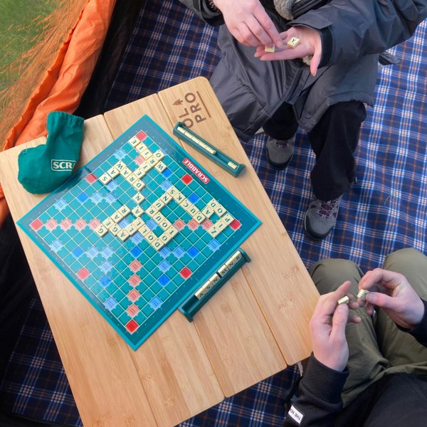 The OLPRO Bamboo Camping Table pictured in a campervan awning with a scrabble board being played with on top of the table.