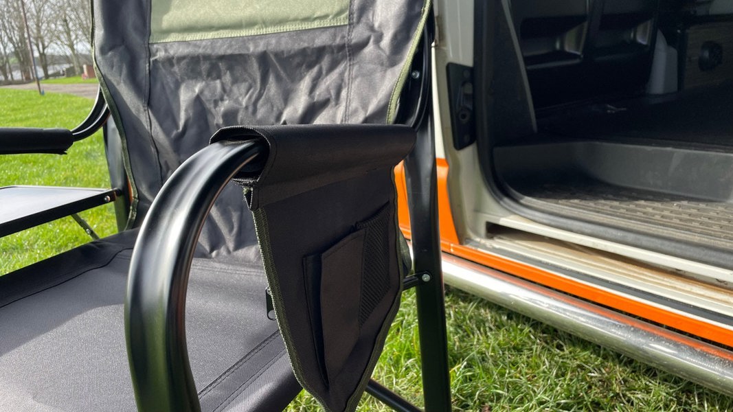 A closeup of the side storage pocket of the OLPRO Directors Camping Chair in green and black in front of a VW Camper Van with its sliding door open.