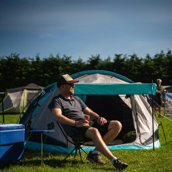 A man sits in an OLPRO camping chair outside his  Stafford 3.0 at a festival, he has a cool box