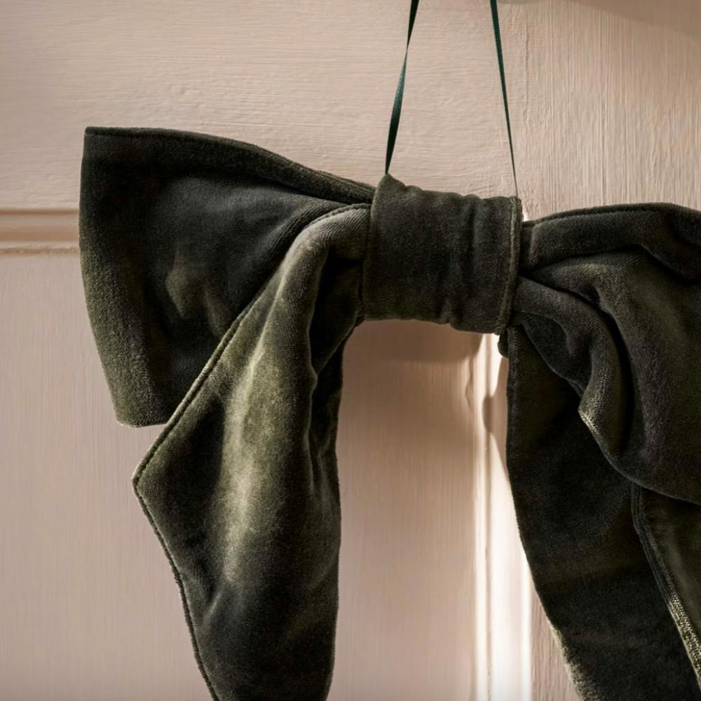 A plush fern green cotton velvet Christmas door bow with a thin hanging loop displayed against a white door.