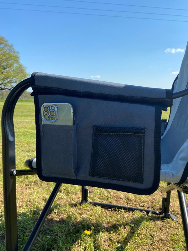 The side storage pocket that contains a mobile phone of the OLPRO Directors Camping Chair in grey being used in a field.