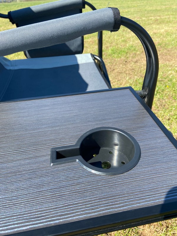 A closeup of the foldable side table being used on the OLPRO Directors Camping Chair in grey being used in a field.