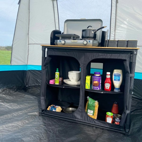 The OLPRO Deluxe Camp Kitchen With Double Cupboard pictured in a kitchen tent with cooking apparatus and food stored inside of it.