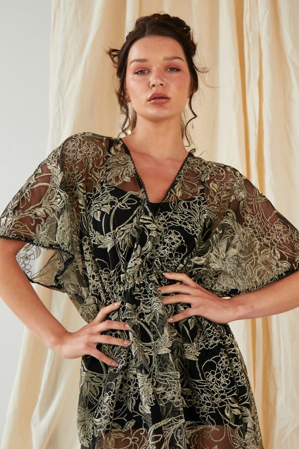 the model is wearing a black and gold embroidered flutter sleeve dress by Sarvin.