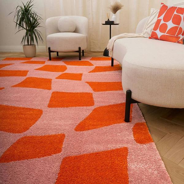 Living room with a pink and orange geometric patterned rug, beige armchair, and sofa with a red pillow.