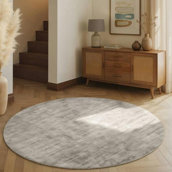 Round gray rug on a wooden floor with a wooden sideboard and decor in the background.