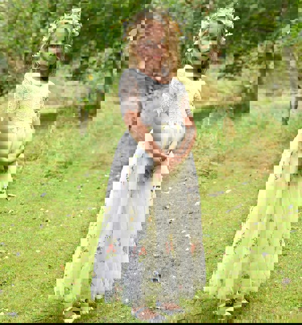 Young girl in a white floral dress standing in a grassy field with trees in the background