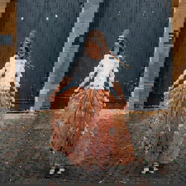 Young girl in a white top and orange floral skirt standing in front of large black doors.