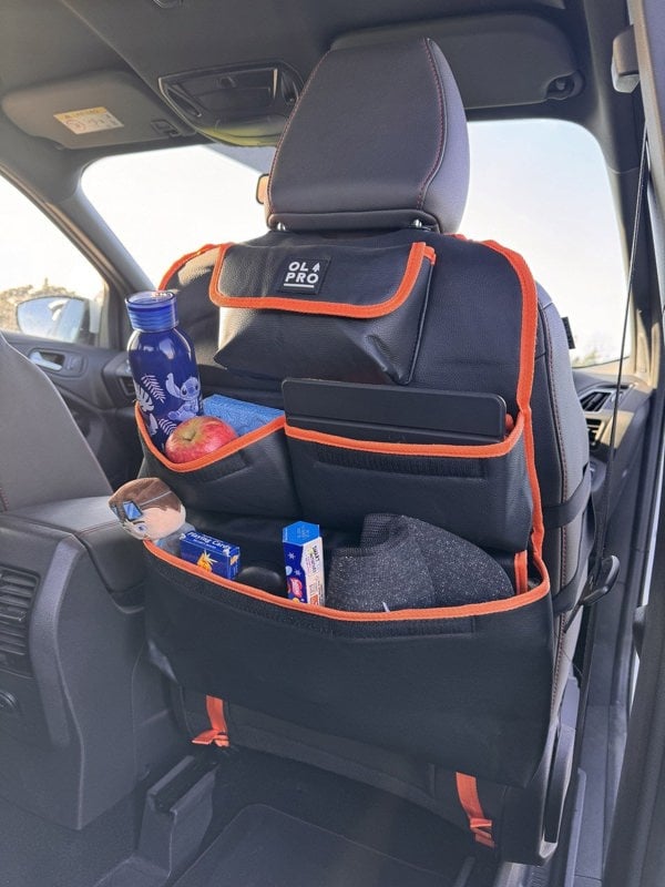 The Rear Single Seat Storage Organiser in Orange by OLPRO attached to the front drivers seat of a VW vehicle full of items for children.