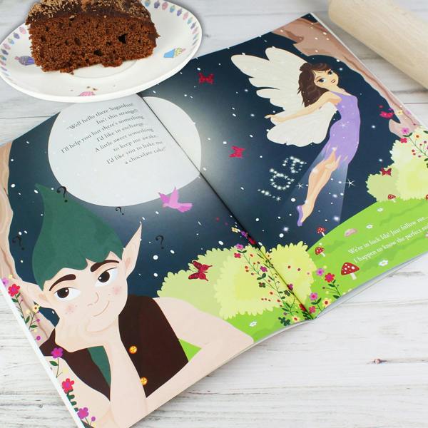 Open view of the Personalised Fairy Baking Adventure storybook showing Sugardust the Fairy floating beside starlight spelling the name Ida, next to a slice of chocolate cake on a plate
