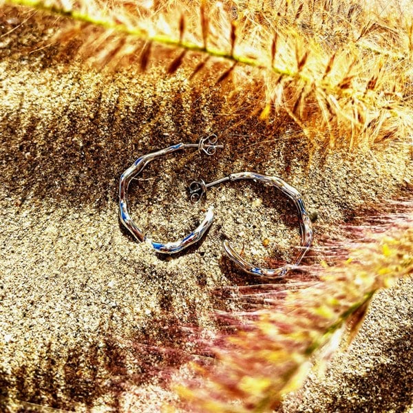Silver hoops with wavy design on sandy background.
