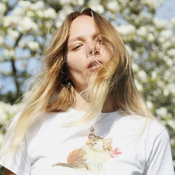 Heart-shaped pearl pendant by LENAE London worn by a blonde model with blossom behind her.