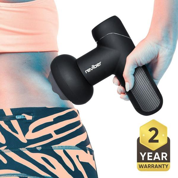 A person uses a black Reviber Active Relief Shiatsu Massager on their lower back for deep tissue relief, wearing a peach sports top and patterned leggings. A 2 Year Warranty badge from Reviber is shown in the bottom right corner.