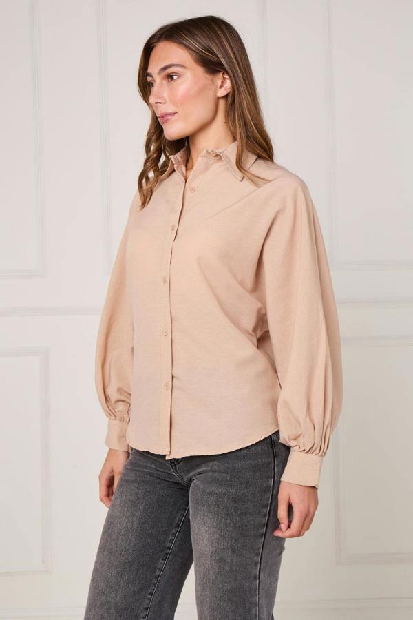 Woman wearing a beige blouse and gray jeans against a white background