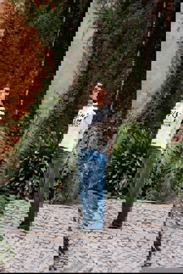 Woman wearing a white sweatshirt with text standing on a stone path with greenery.