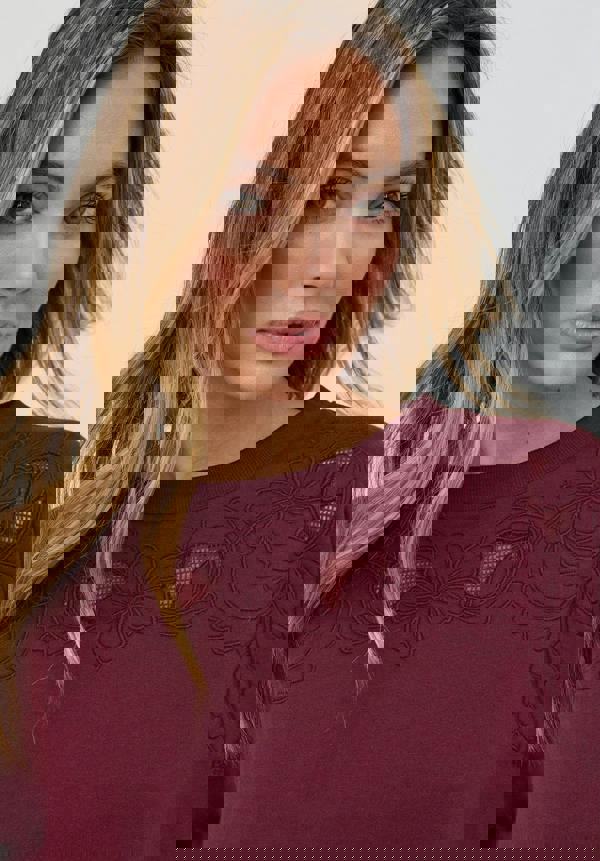 Woman wearing a burgundy top with floral lace details against a white background