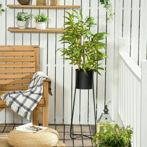Artificial bamboo tree with green leaves in black pot on a tall stand in outdoor-style setting