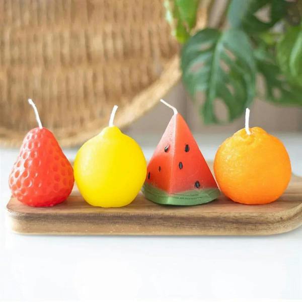Set of four fruit-shaped candles: strawberry, lemon, watermelon slice, orange on tray.