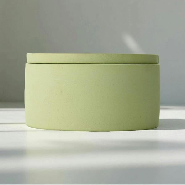 Green cylindrical container with a lid on a reflective surface with a blurred background