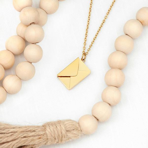 A closed gold envelope pendant necklace from Abode Home & Gifts displayed flatlay inside a loop of large wooden garland beads.