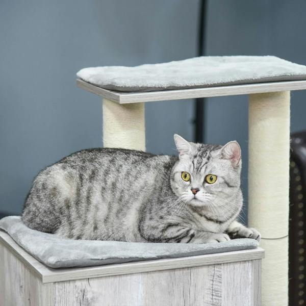 Grey striped cat lying on a grey cushioned perch of a multi-level cat tree