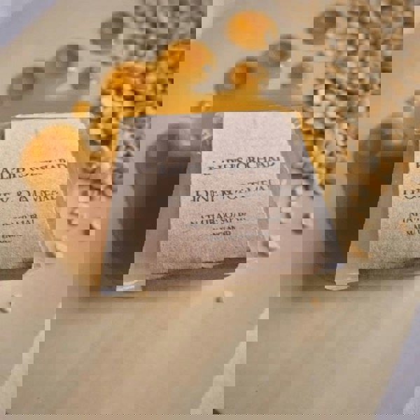 Soap bar labeled 'Ralph's Orchard Honey & Oatmeal' with honey and oats on a wooden surface.