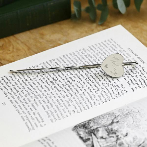 A polished silver-coloured heart bookmark engraved with the name Sophia in script text, marking a page inside an open book.