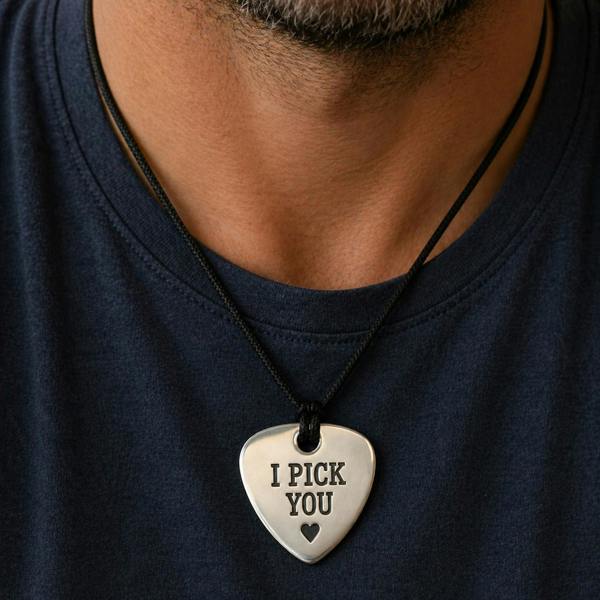 A close-up view of a man's neck and chest wearing a navy blue t-shirt and a silver plectrum necklace engraved with 'I PICK YOU'.