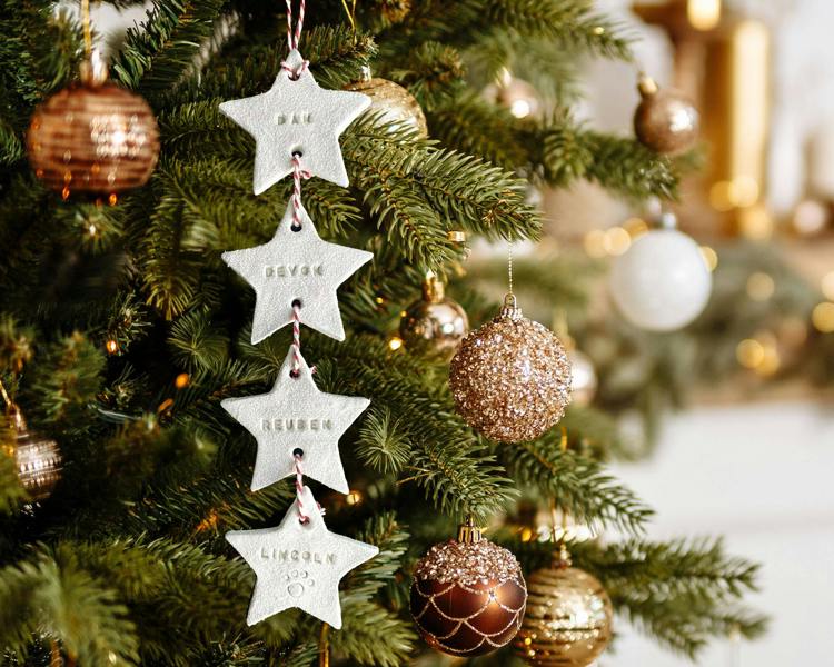 A cascading Personalised Family Christmas Decoration with hand-stamped star tags for Dan, Devon, Reuben, and Lincoln hanging on a lit tree.