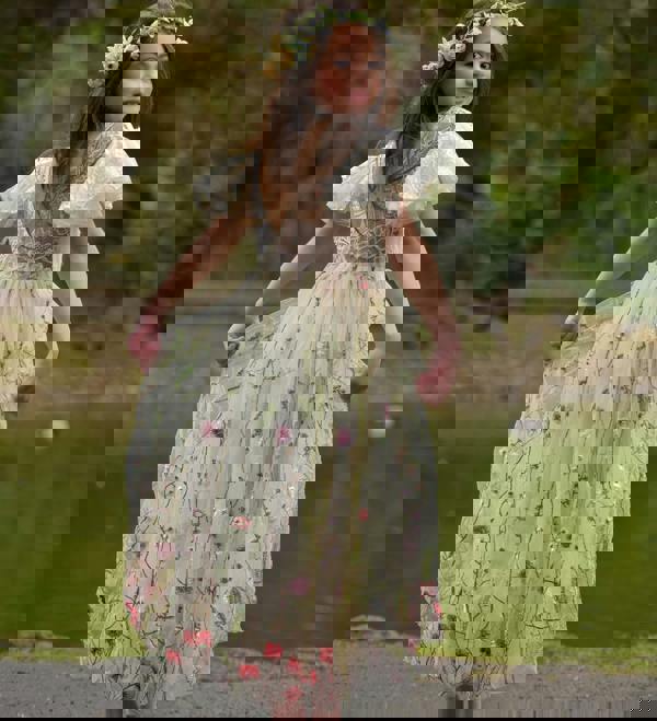 Young girl in a floral dress standing by a pond with greenery in the background