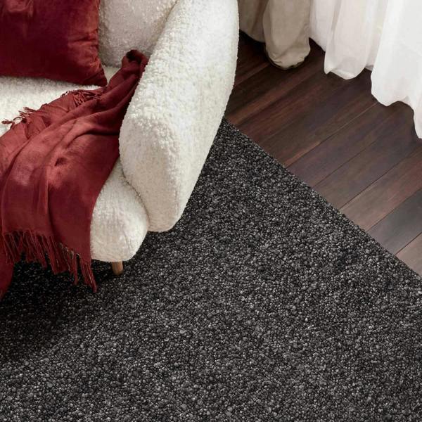 Close-up of a dark gray carpet with a white chair and red blanket in the background.