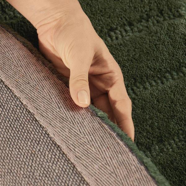 Hand touching the edge of a green textured rug with a brown border