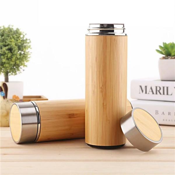 Eco-friendly bamboo travel mug with a stainless steel lid and internal tea infuser, standing on a wooden surface next to a white book.