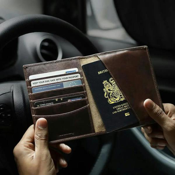 Person holding a brown leather wallet with a British passport inside, car interior background