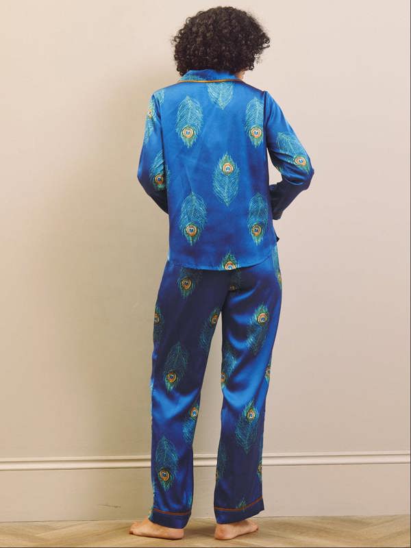 Person wearing blue pajama set with peacock feather pattern on a beige wall background