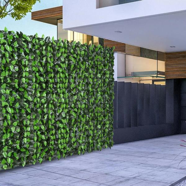 Artificial leaf hedge privacy fence panel with dense green leaves along an outdoor walkway