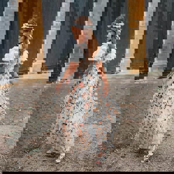 Young girl in a floral dress standing in front of a brick building.