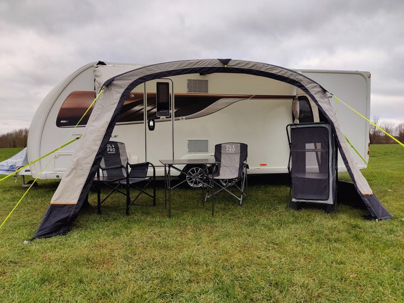 The OLPRO View Lite Breeze 390 Caravan Awning pictured in a Caravan site attached to a caravan with  some camping furniture on display inside of the awning.