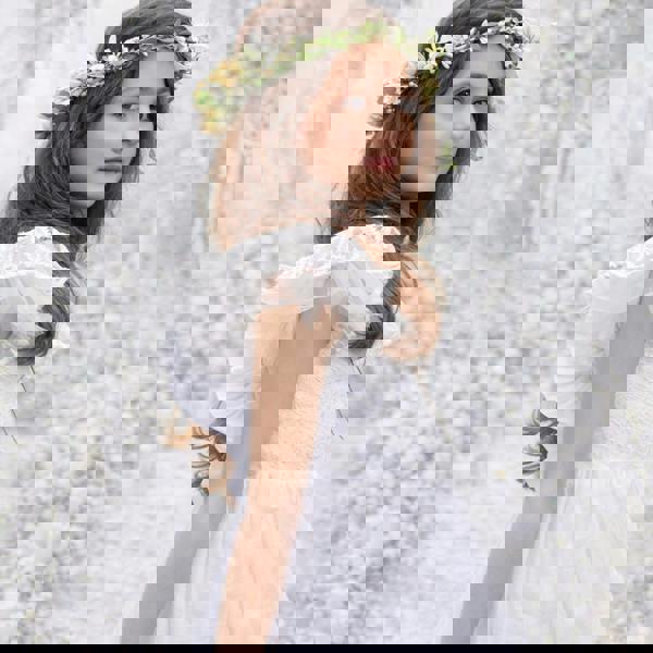 Young girl in a white dress with a floral headband against a textured white background