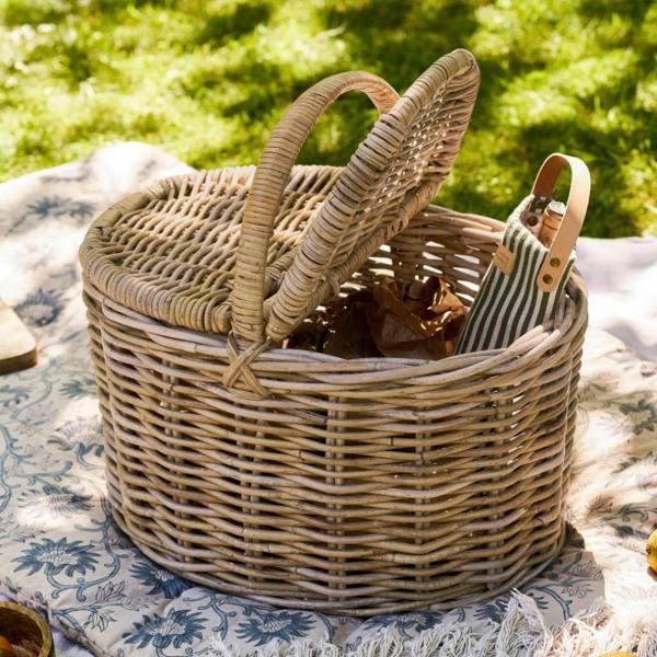 Woven rattan picnic basket sitting on a floral blanket in a sunny garden.