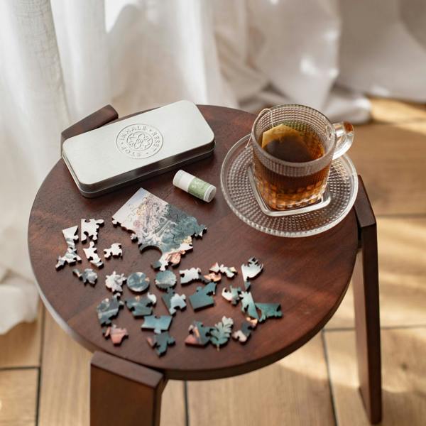 Wooden table with a puzzle, phone, and cup of tea on a wooden floor.