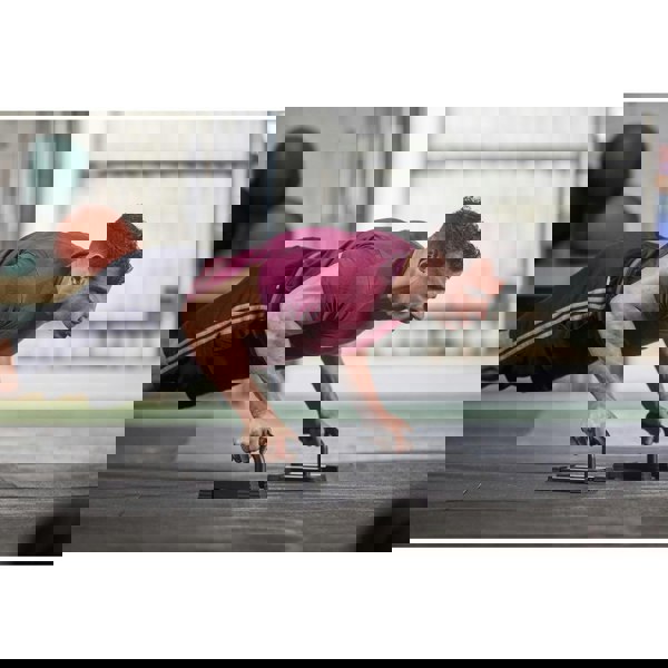 Man performing push-ups using the Adidas Premium Push Up Bars with gym equipment in the background