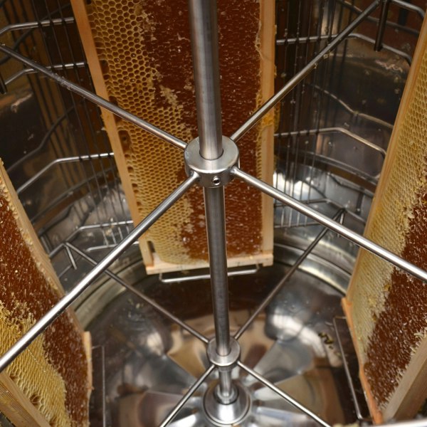 Electric honey extractor with stainless steel frame, holding honeycomb frames, showcasing a shiny, polished interior and sturdy construction