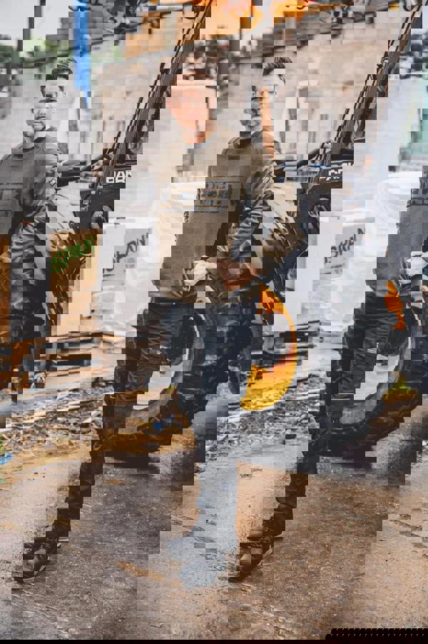 JCB Crew Trade Mens Work Pull Over Sweat Shirt, male worker wearing olive green sweatshirt with black accents in construction yard with tractor and building materials.