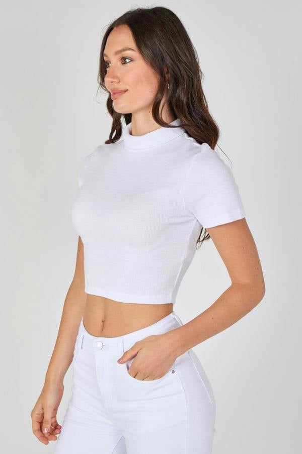 Woman wearing a white crop top and white pants against a plain background