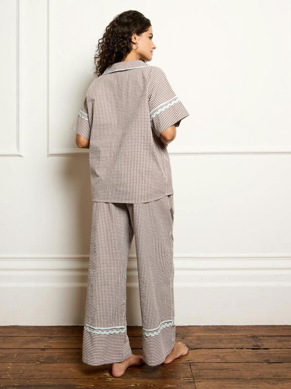 Woman wearing a gingham pyjama set against a white wall.
