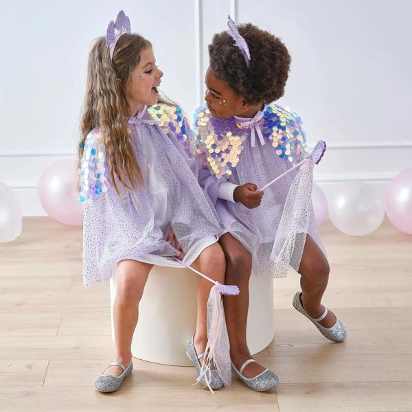 Two young girls sitting together at a party playing in matching purple sequin mermaid costume capes with crowns and magic wands.