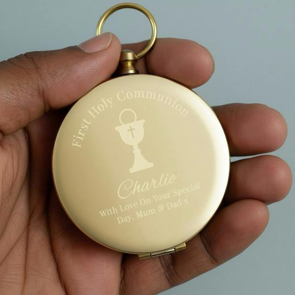 A hand holding the gold-toned Personalised First Holy Communion Compass engraved with Charlie and a chalice motif.