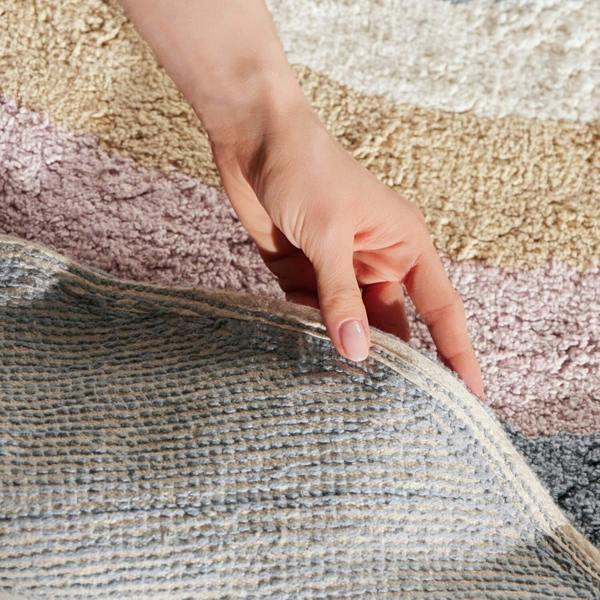 Hand touching the edge of a textured rug with a multicolored background