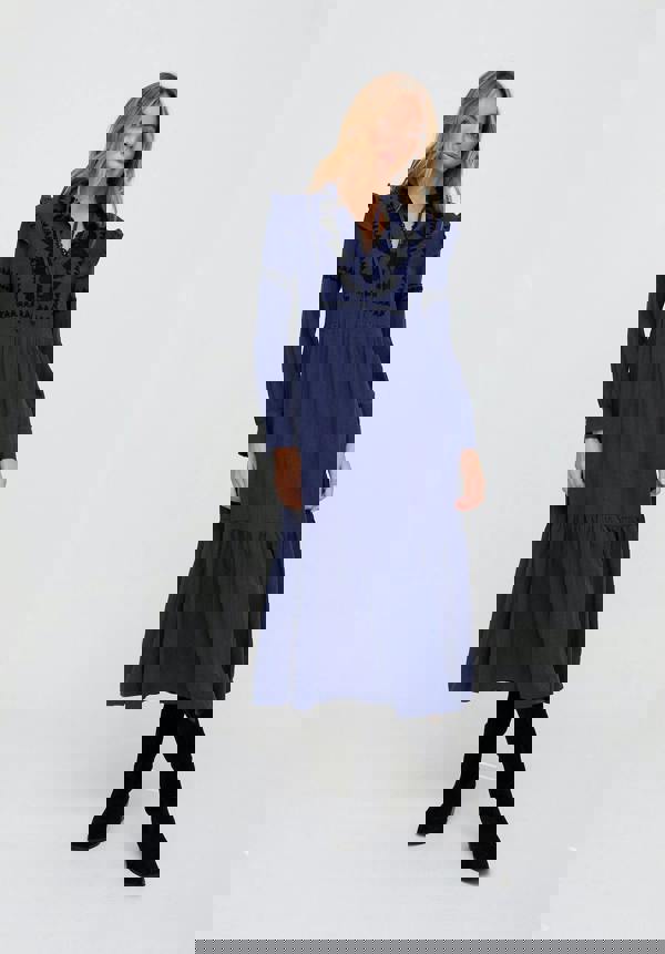 Woman wearing a blue dress with black embroidery on a white background